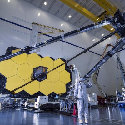 A person in a hazmat suit standing beneath a large telescope.